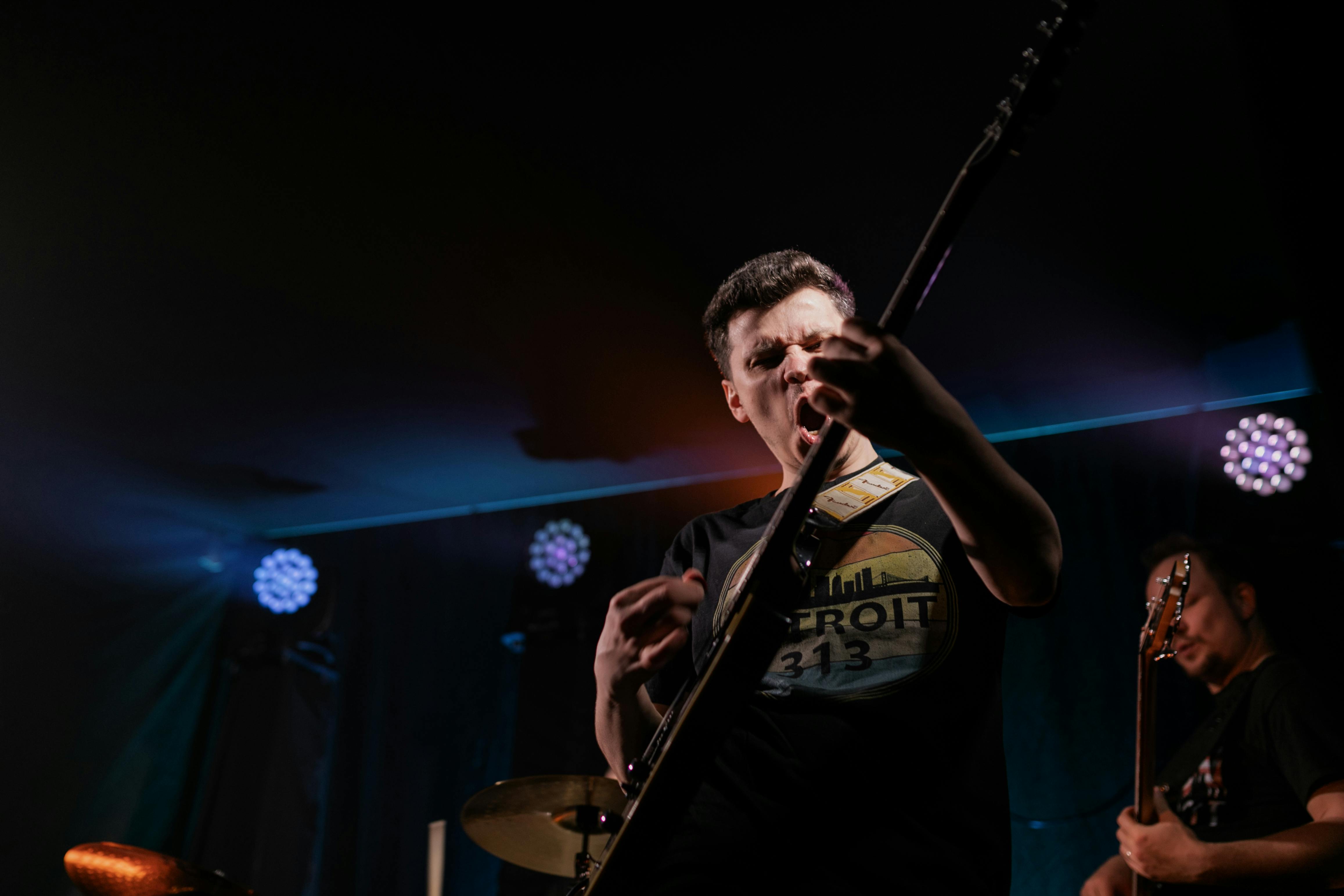 Guitarist performing with intense energy on stage with dramatic stage lighting